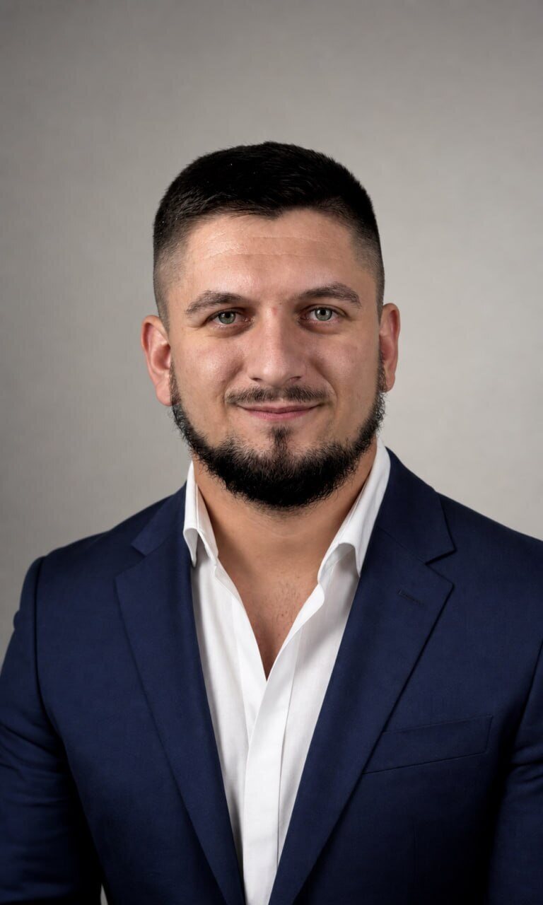 Esef Cosic, photographed against a plain grey background in a navy jacket and open white shirt.